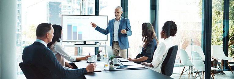 a senior manager presenting stats on a screen in a office board room